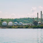 Vista de uma instalação industrial costeira de armazenamento de gás, com tanques esféricos e chaminés.