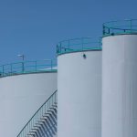 Tanques industriais de armazenamento com estruturas verdes sob céu azul.
