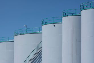 Tanques industriais de armazenamento com estruturas verdes sob céu azul.