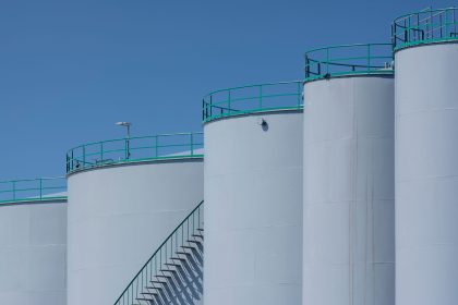 Tanques industriais de armazenamento com estruturas verdes sob céu azul.