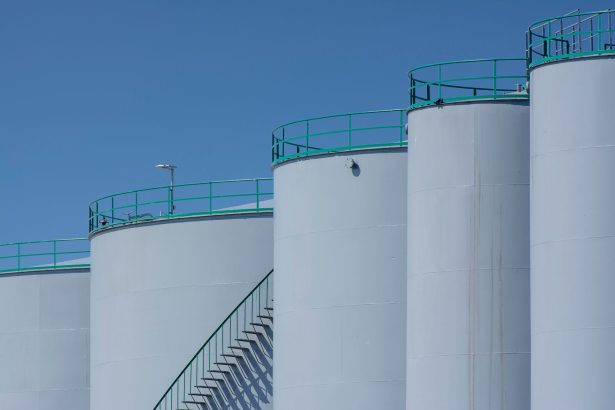 Tanques industriais de armazenamento com estruturas verdes sob céu azul.