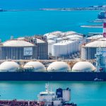 Vista aérea de um terminal de gás natural liquefeito, com tanques de armazenamento e navios-tanque junto à costa.