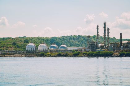 Vista de uma instalação industrial costeira de armazenamento de gás, com tanques esféricos e chaminés.