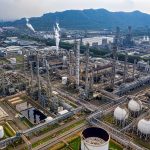 Vista aérea de um complexo de refino de petróleo com tanques de armazenamento e tubulações industriais.