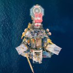 Vista aérea de uma plataforma de petróleo em alto-mar, cercada pelo oceano.
