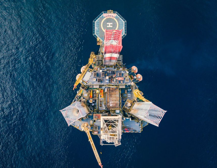 Vista aérea de uma plataforma de petróleo em alto-mar, cercada pelo oceano.