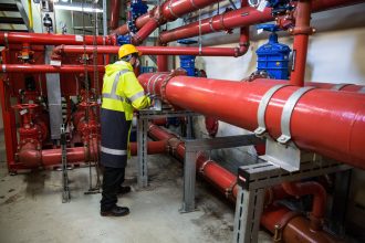 Profissional com equipamento de segurança inspeciona tubulações industriais em uma instalação de processamento de biogás.