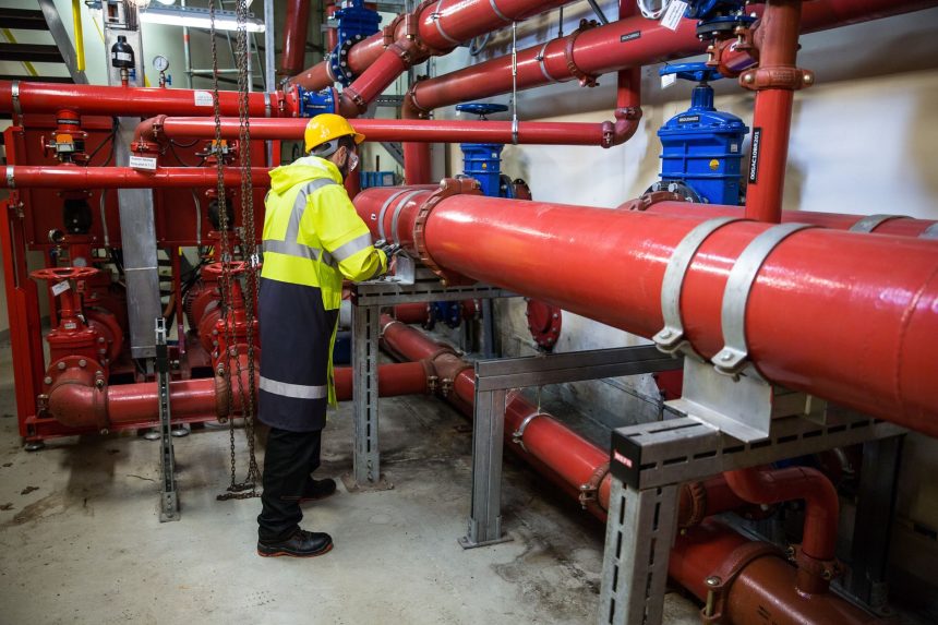 Profissional com equipamento de segurança inspeciona tubulações industriais em uma instalação de processamento de biogás.