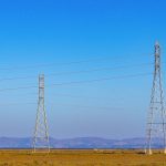 Torres de transmissão e linhas de energia elétrica em uma paisagem natural sob céu azul.