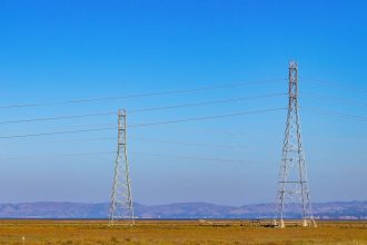 Torres de transmissão e linhas de energia elétrica em uma paisagem natural sob céu azul.