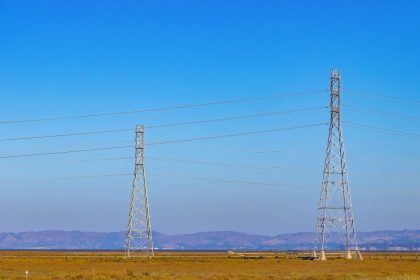 Torres de transmissão e linhas de energia elétrica em uma paisagem natural sob céu azul.