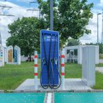 Estação pública de recarga para veículos elétricos em ambiente urbano, com área arborizada ao redor.