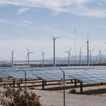 Parque de energia renovável com aerogeradores e painéis solares sob céu aberto.