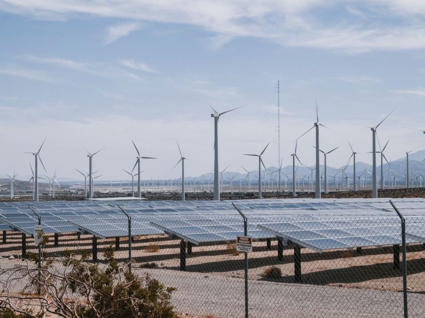Parque de energia renovável com aerogeradores e painéis solares sob céu aberto.