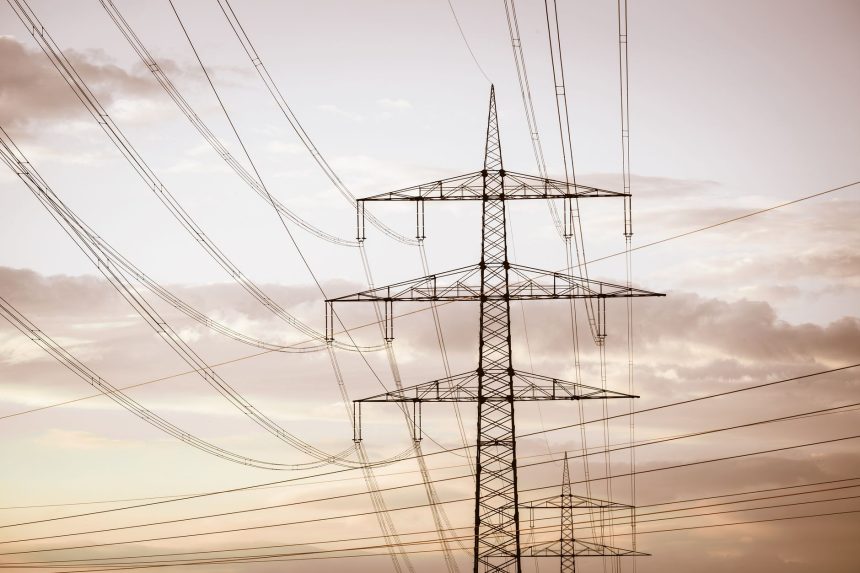 Torres e linhas de transmissão de energia elétrica em silhueta diante de um céu colorido ao entardecer.